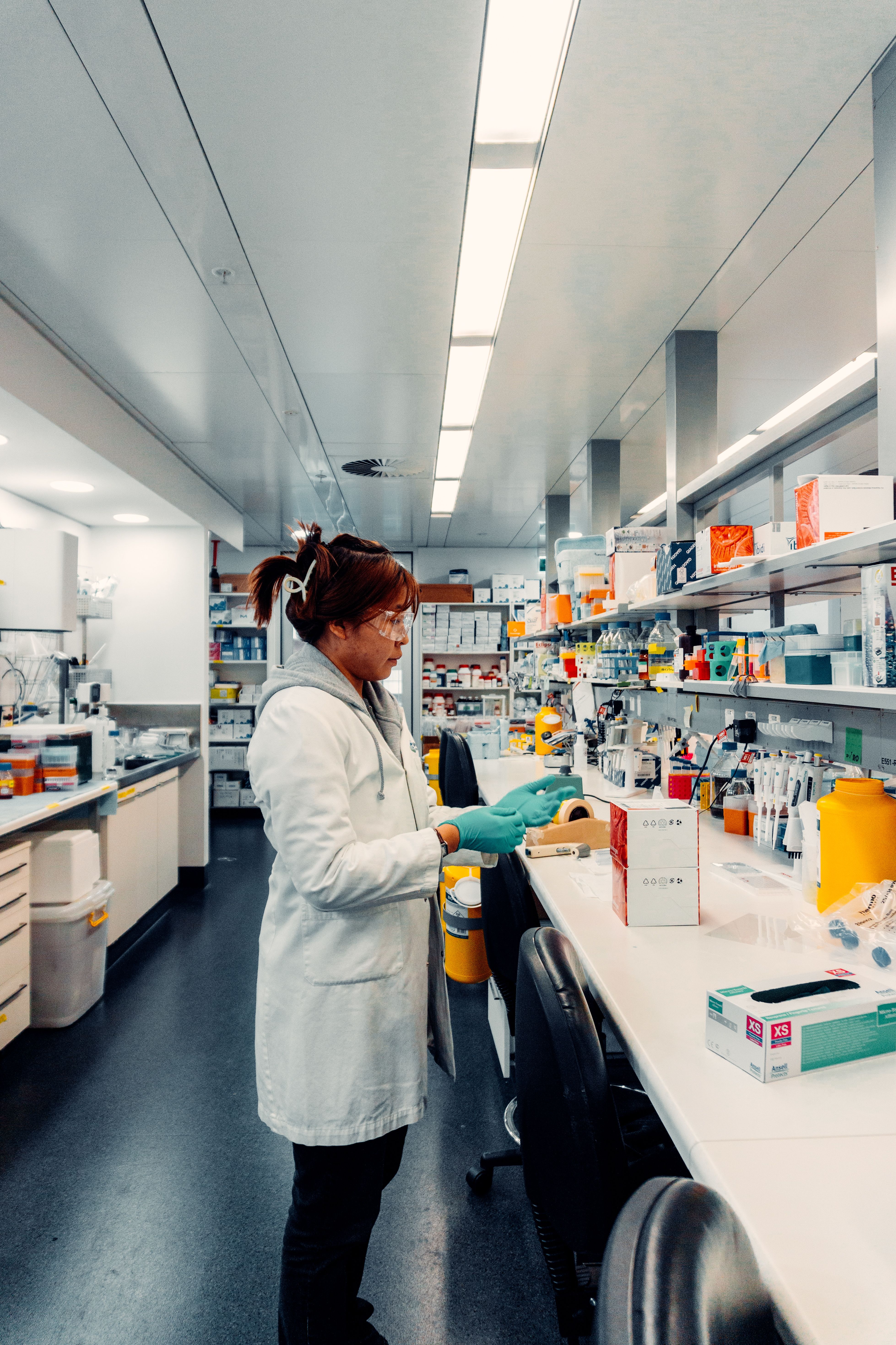 A young woman wearing a lab coat and protective lab glasses captured whilst working in the lab.