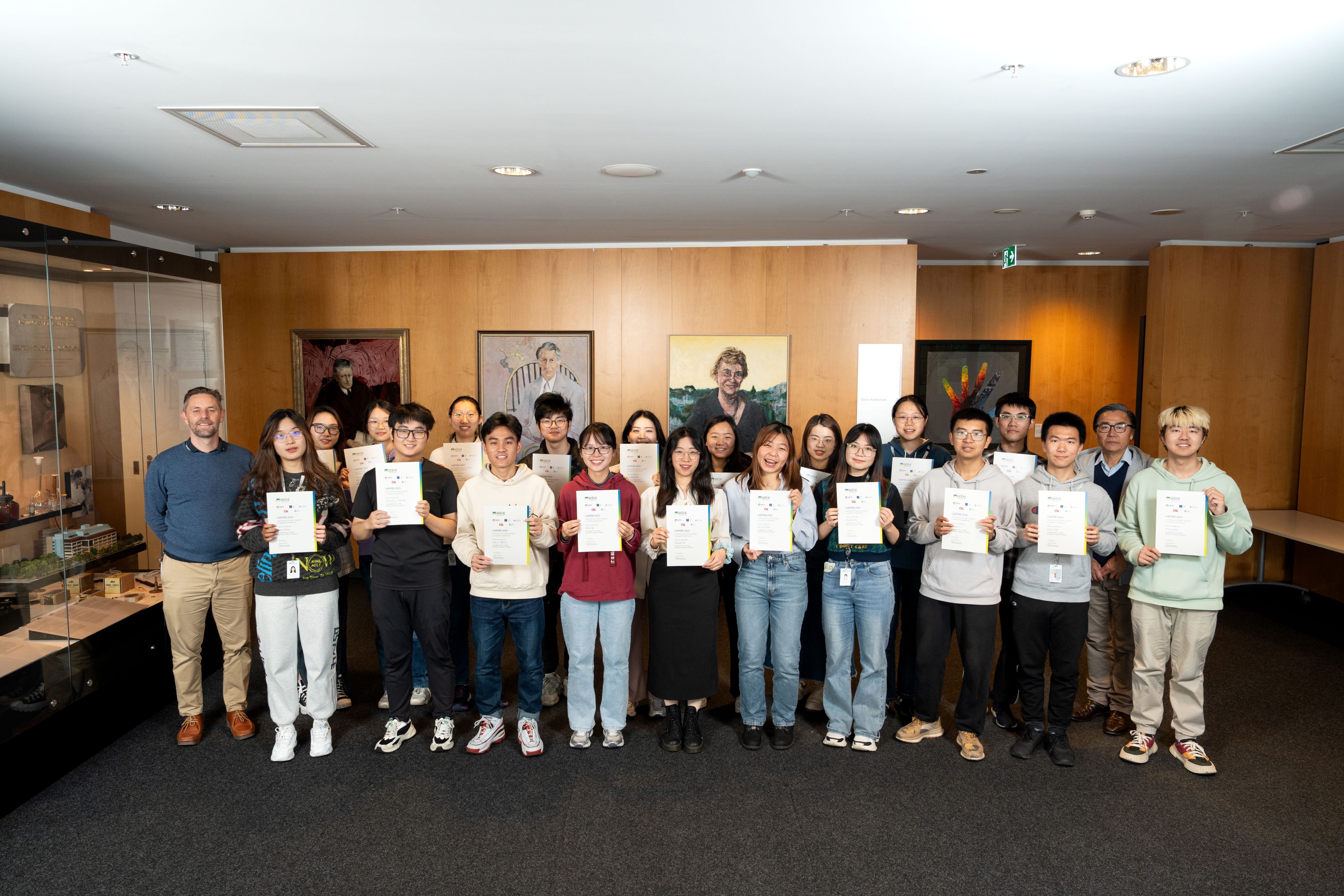 A man standing on the left with a group of several university students posing for a group photo, each holding a certificate.  